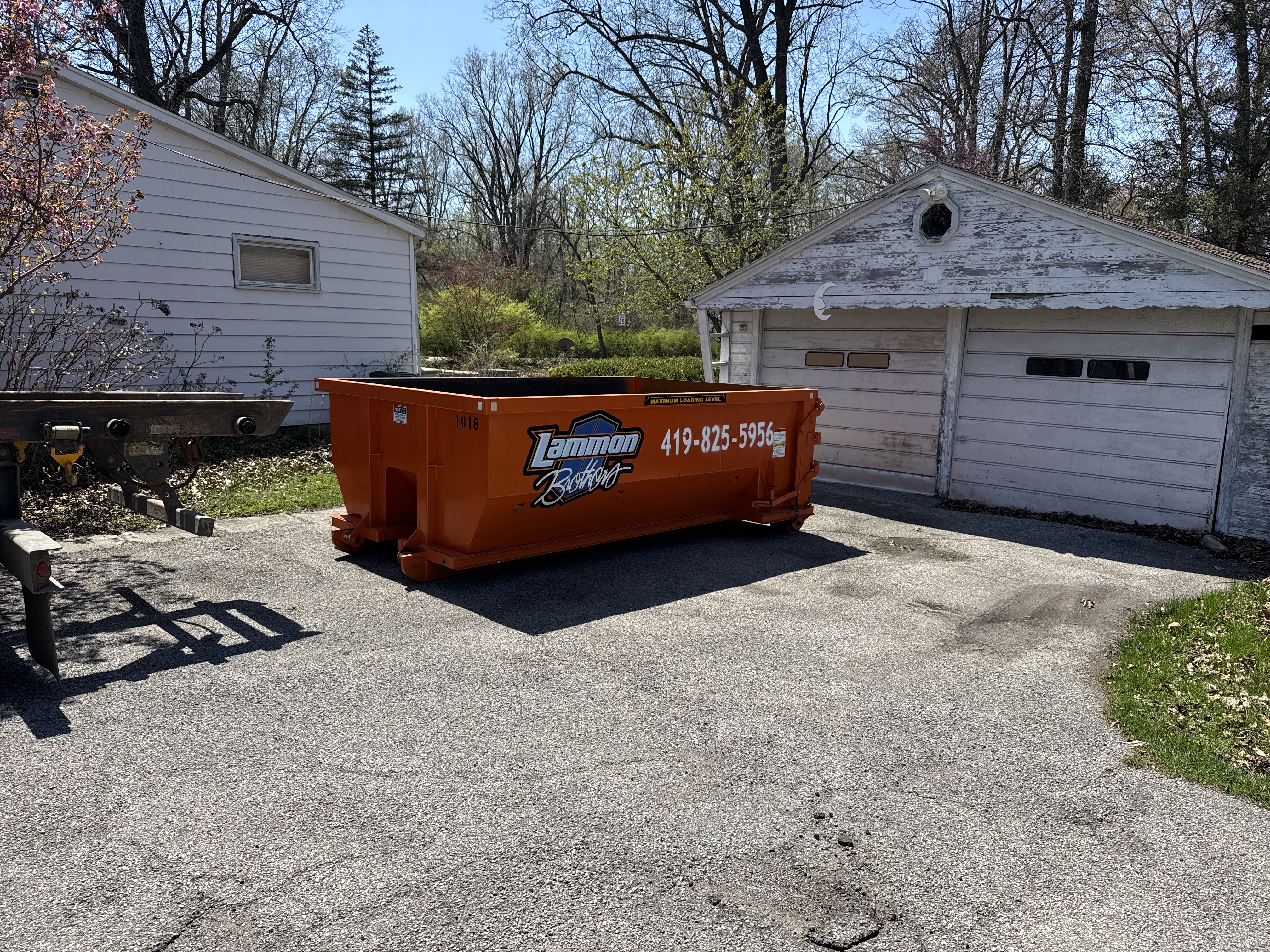 Orange Lammon Bros roll-off dumpster being delivered to a paved surface