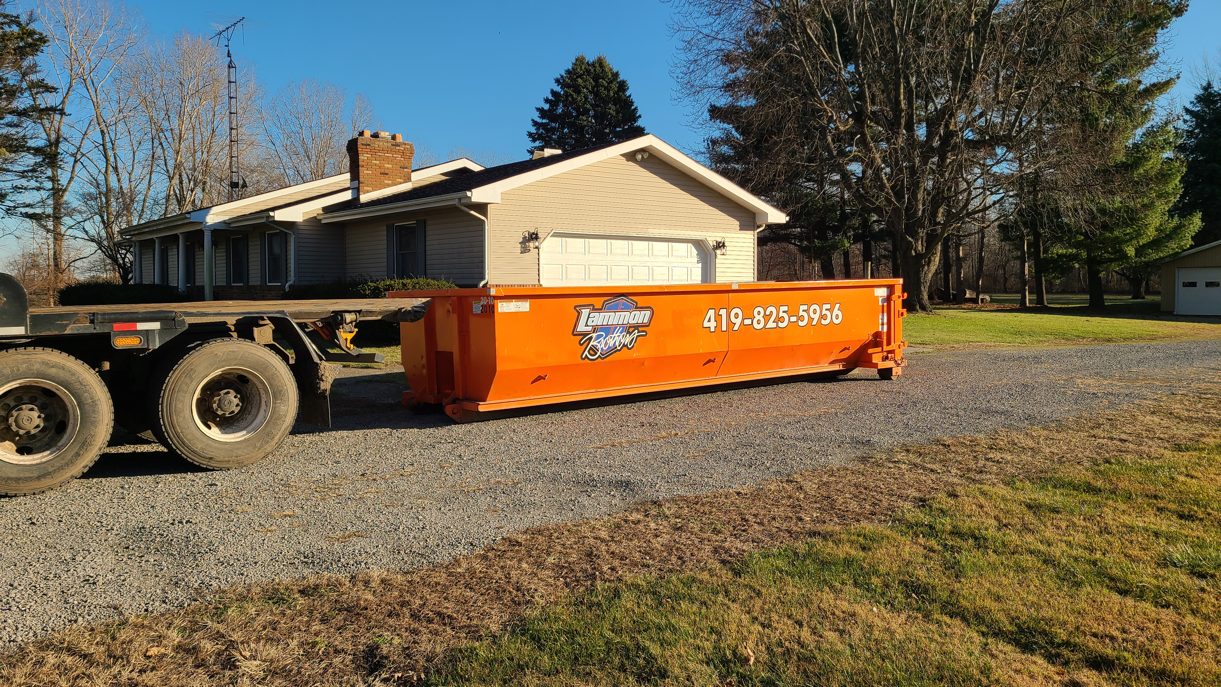 Lammon Bros roll-off truck delivering an orange dumpster in Napoleon