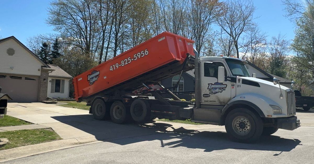 White Kenworth Lammon Bros truck tilting an orange roll-off dumpster off the bed