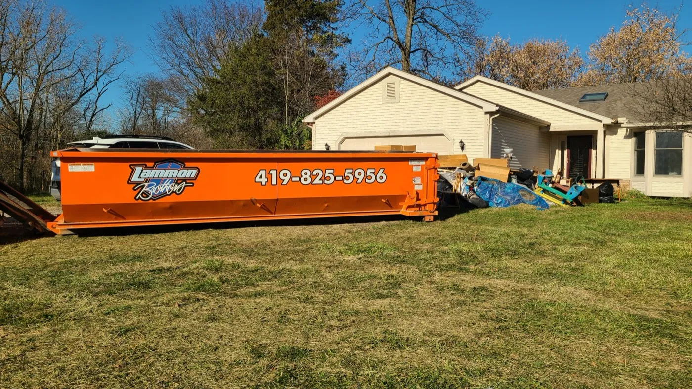 Orange Lammon Bros roll-off dumpster on a grassy lawn beside a tan house