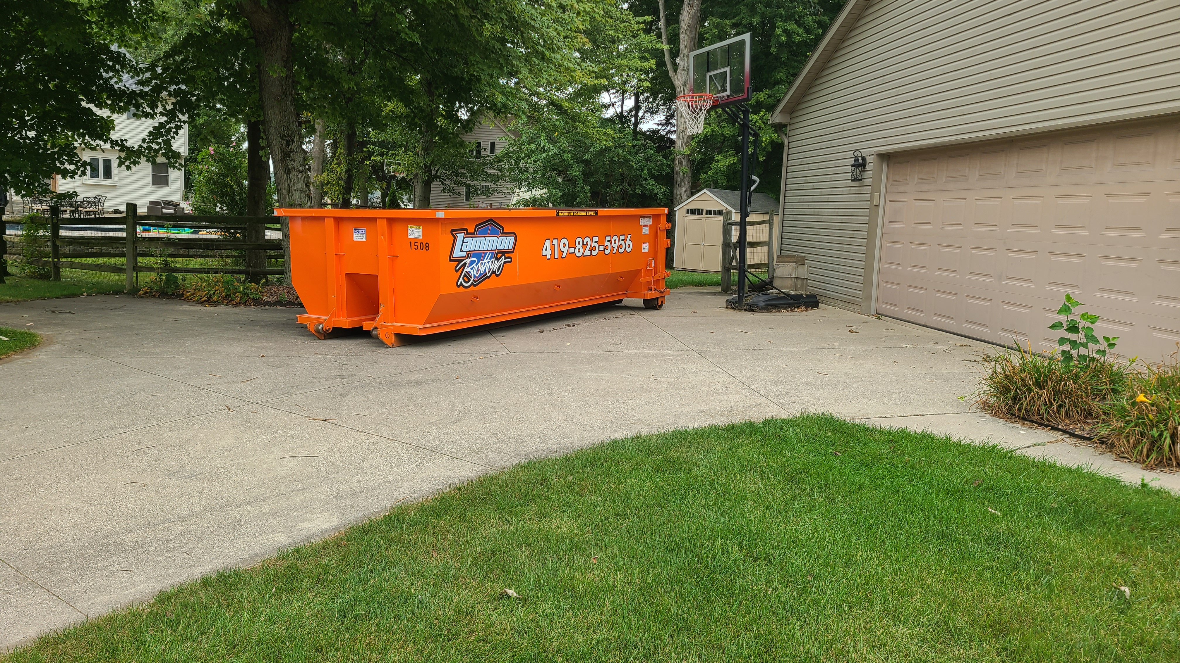 Orange Lammon Bros roll-off dumpster on a wide concrete driveway