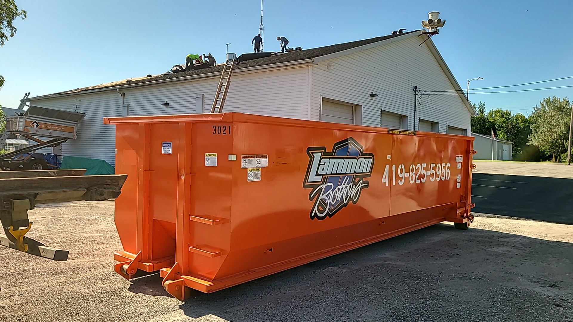 Orange Lammon Bros roll-off dumpster staged on a gravel lot