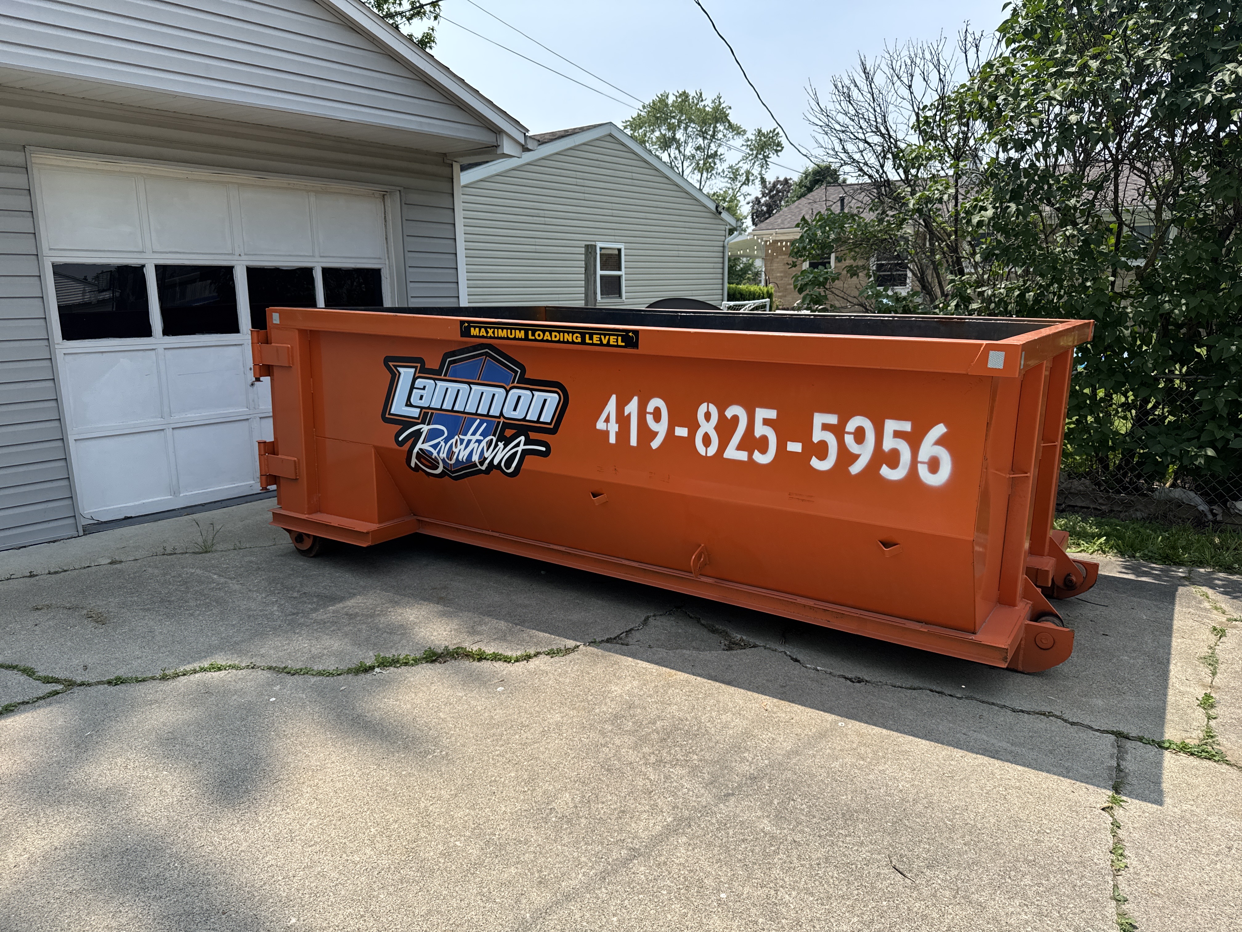 Empty orange Lammon Bros roll-off dumpster parked on concrete
