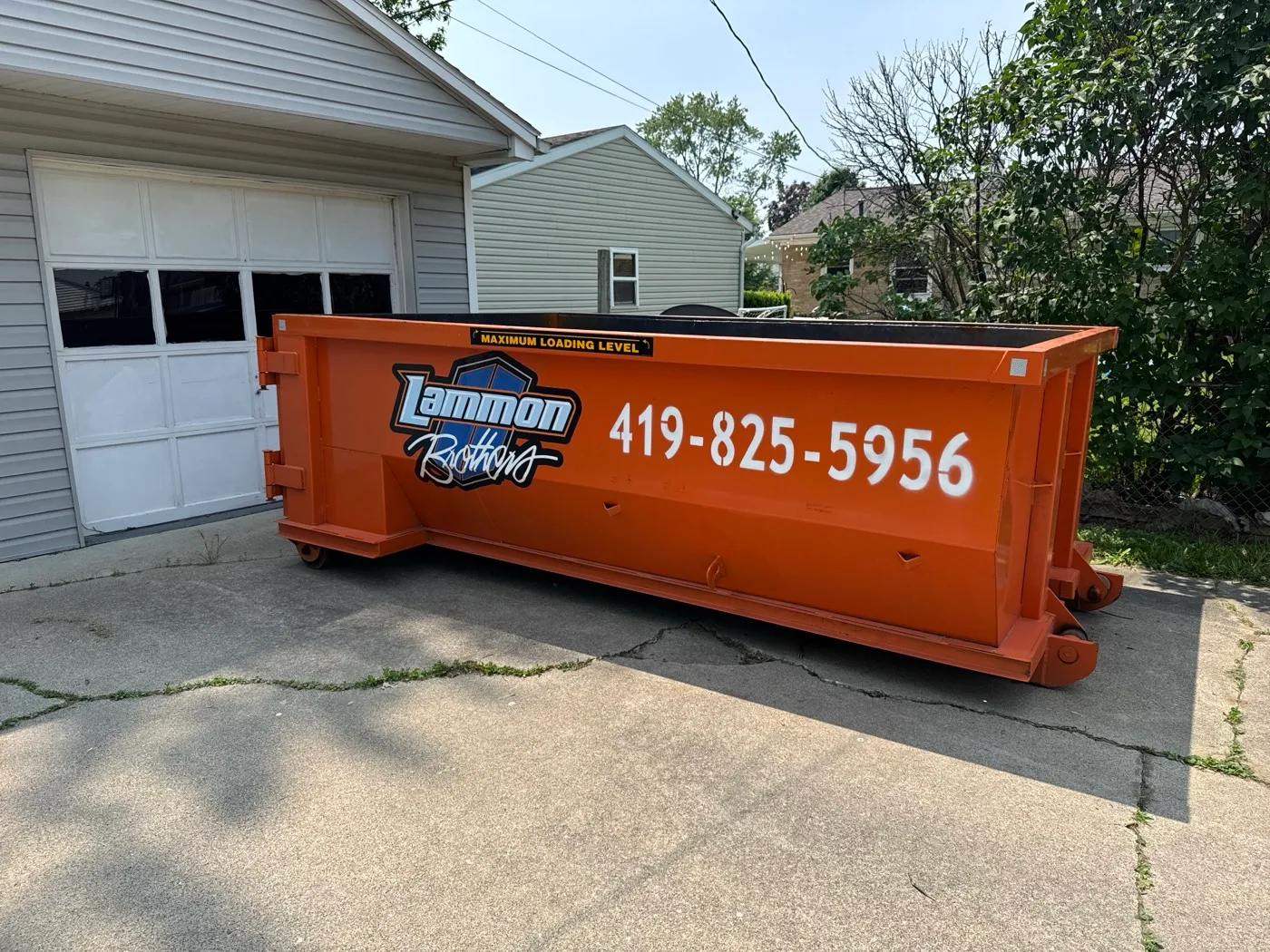 Empty orange Lammon Bros roll-off dumpster parked on concrete