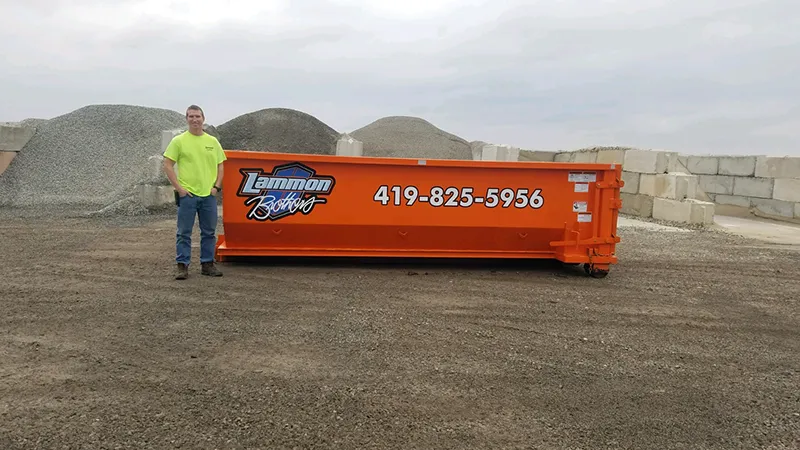Owner standing beside an orange 15-yard Lammon Bros dumpster for scale