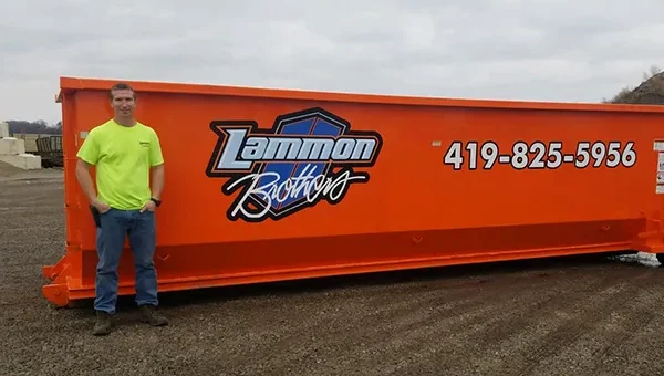 Owner standing beside an orange 40-yard Lammon Bros dumpster for scale