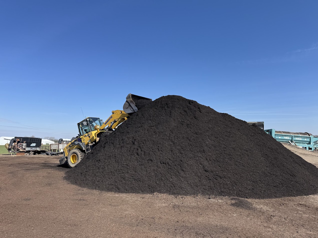 Wheel loader pushing up a large pile of black mulch at the Lammon Bros yard