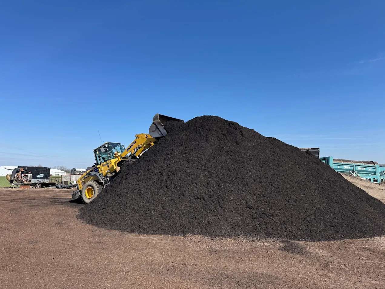Wheel loader pushing up a large pile of black mulch at the Lammon Bros materials yard