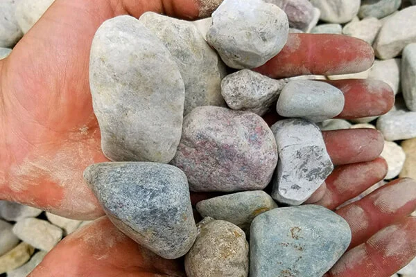 Hands holding medium river rock over a river rock pile