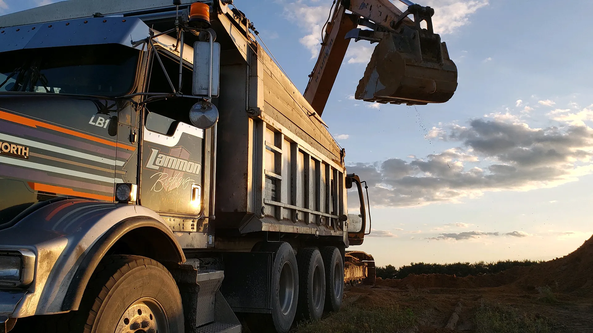 Chrome Lammon Bros Kenworth dump truck being loaded at golden hour