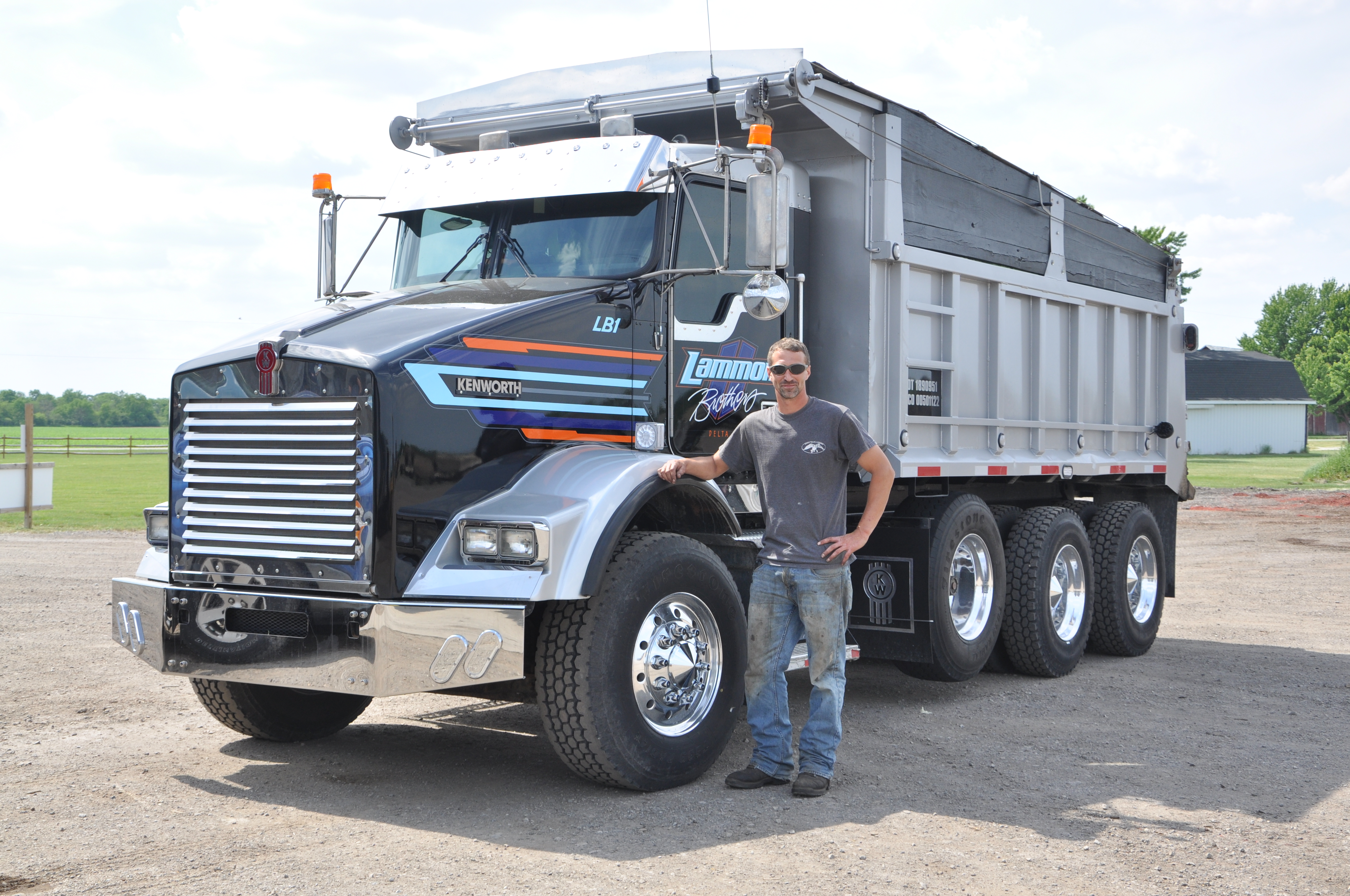A Lammon Brothers crew member in a company t-shirt beside a dump truck at the yard