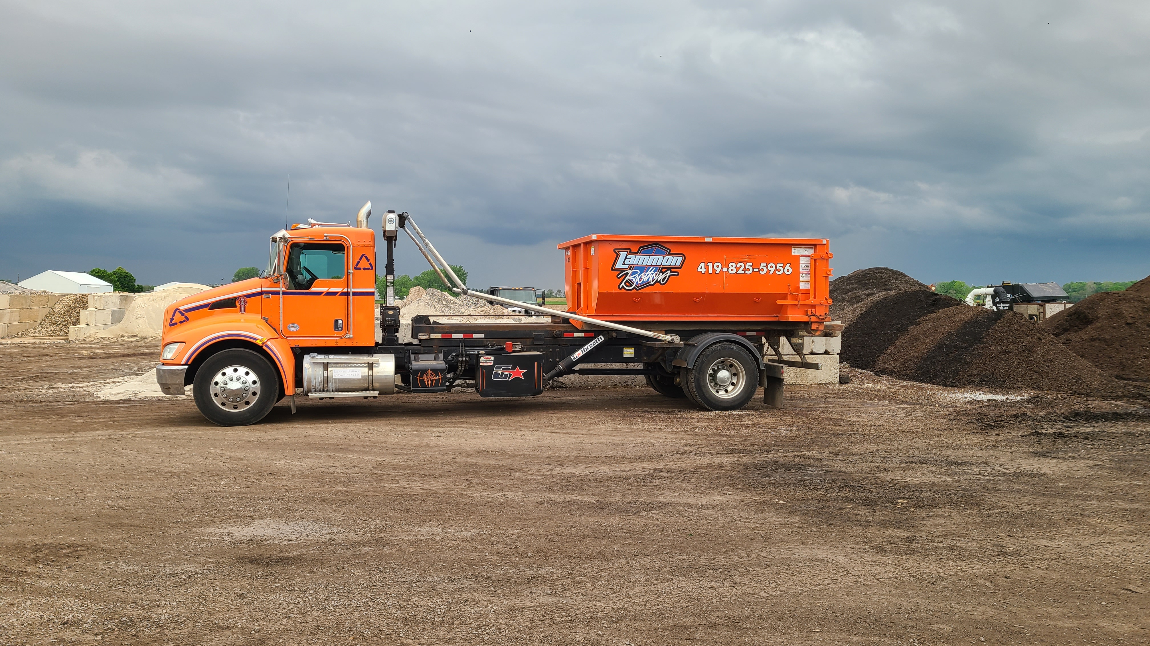 Orange Lammon Bros roll-off truck carrying a dumpster out to Waterville