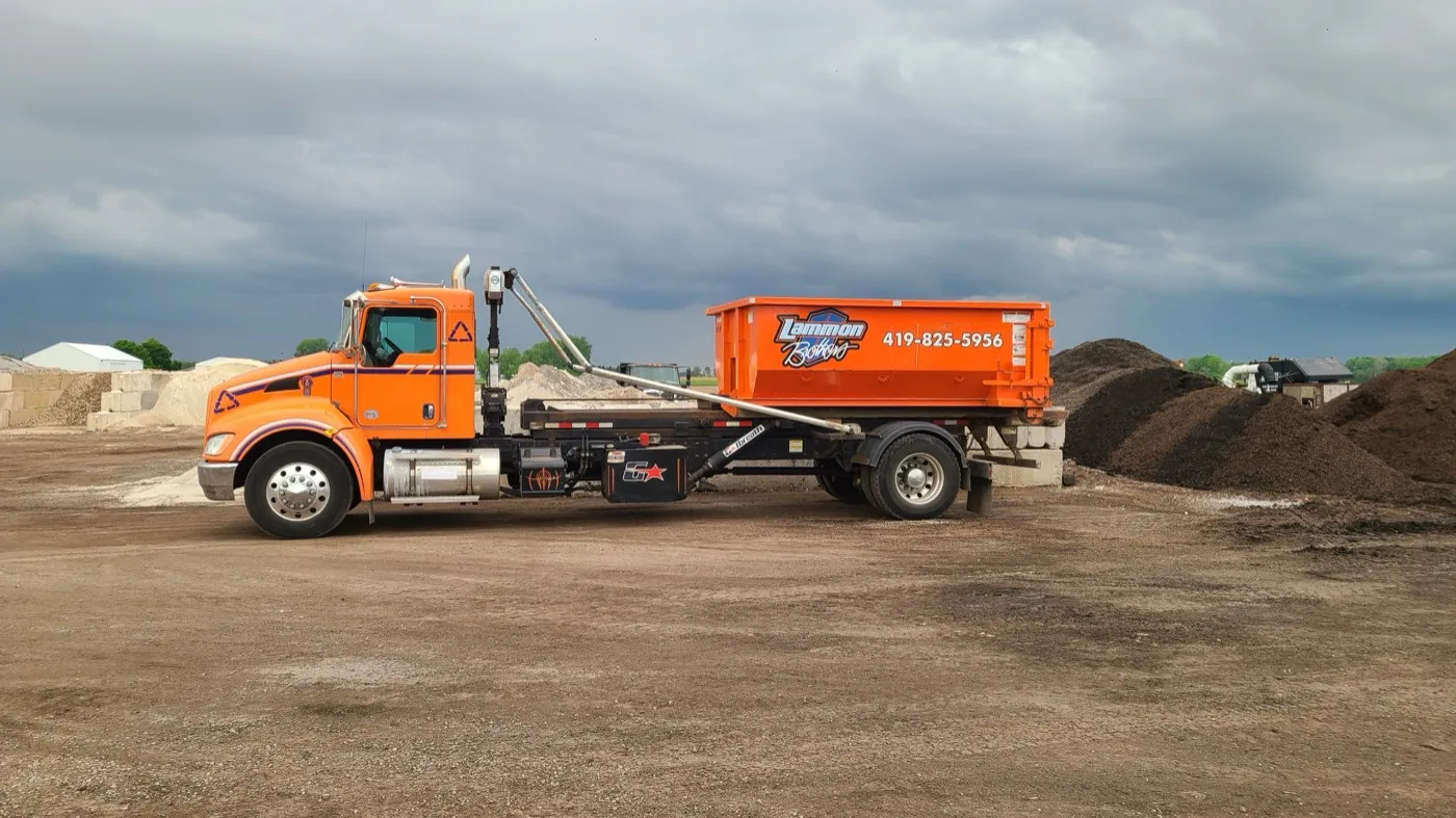 Orange Lammon Bros roll-off truck carrying a dumpster out to Waterville