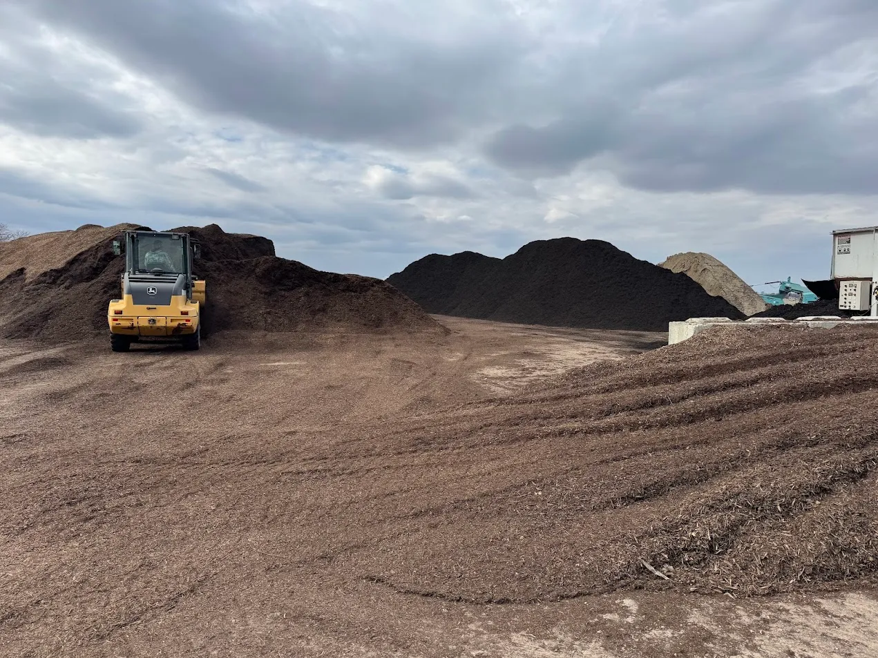 Lammon Bros material yard with bulk piles and a John Deere loader