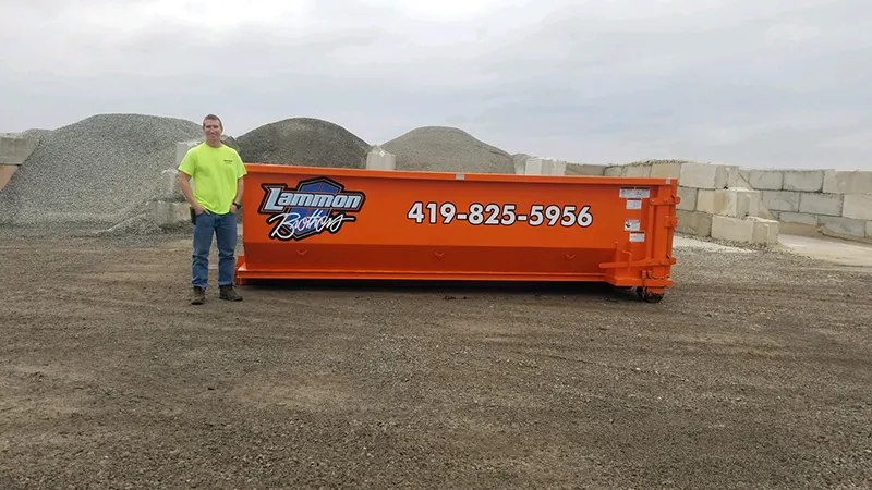 Orange 15-yard dumpster available for rent in Toledo, Ohio, placed on a flat area. A man is standing next to the dumpster to provide a visual representation of its size and volume. Suitable for medium-sized construction, renovation, or cleanout projects.