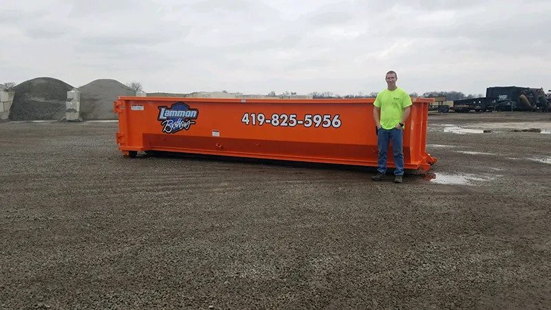 Orange 30-yard dumpster situated in a yard in Toledo, Ohio, available for rent. A man stands next to the container, providing a scale for its large size and extensive volume. Ideal for significant construction endeavors, comprehensive home remodels, or extensive landscaping projects.